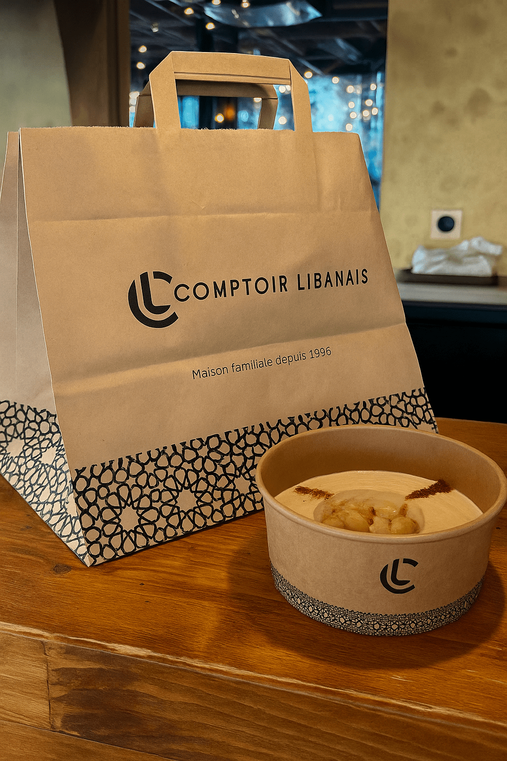 Sac en papier kraft et bol alimentaire personnalisés au logo du Comptoir Libanais, présentés sur un comptoir de restaurant pour les repas à emporter.
