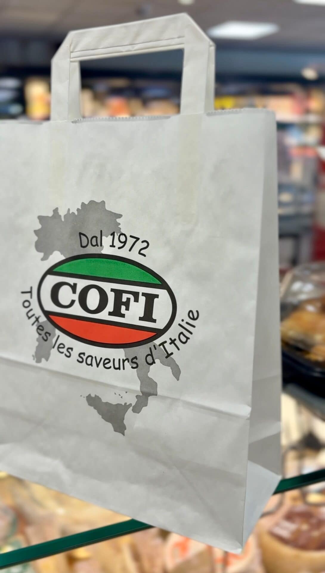 Sac en papier personnalisé du traiteur italien COFI, orné du logo aux couleurs de l’Italie et du texte “Toutes les saveurs d’Italie depuis 1972”.