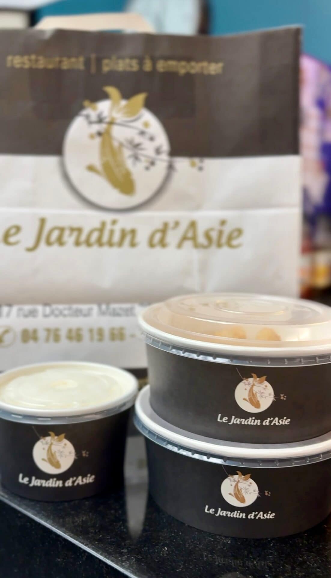 Bols alimentaires noirs avec couvercles transparents et sac kraft assorti, personnalisés au logo du restaurant Le Jardin d’Asie, illustrant un exemple d’emballage de restauration élégant et cohérent pour la vente à emporter.